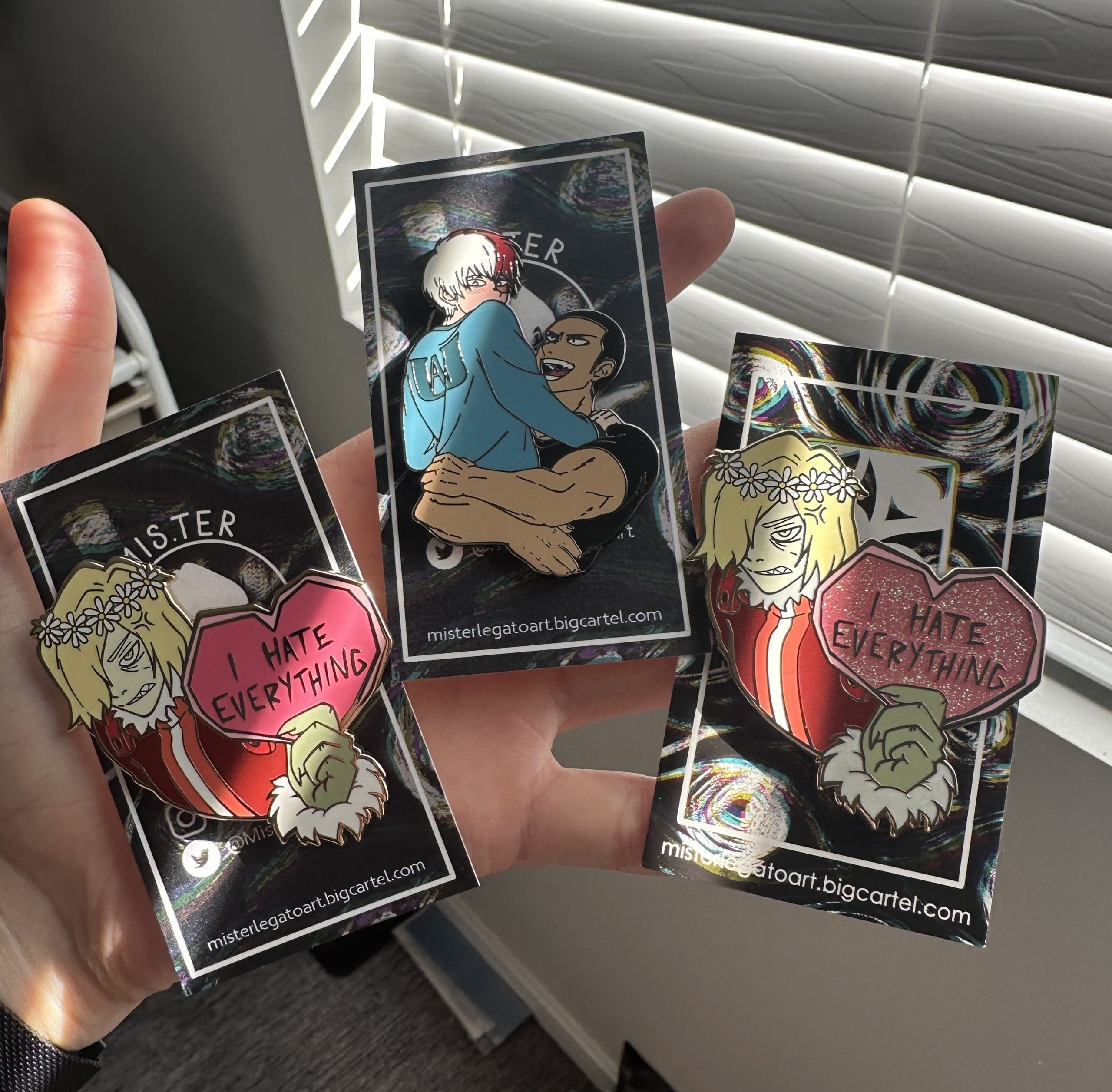 Three enamel pins on someone's hand